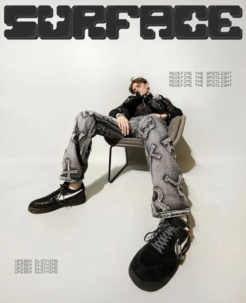 A model seated on a plinth in grey denim, the wordmark above.