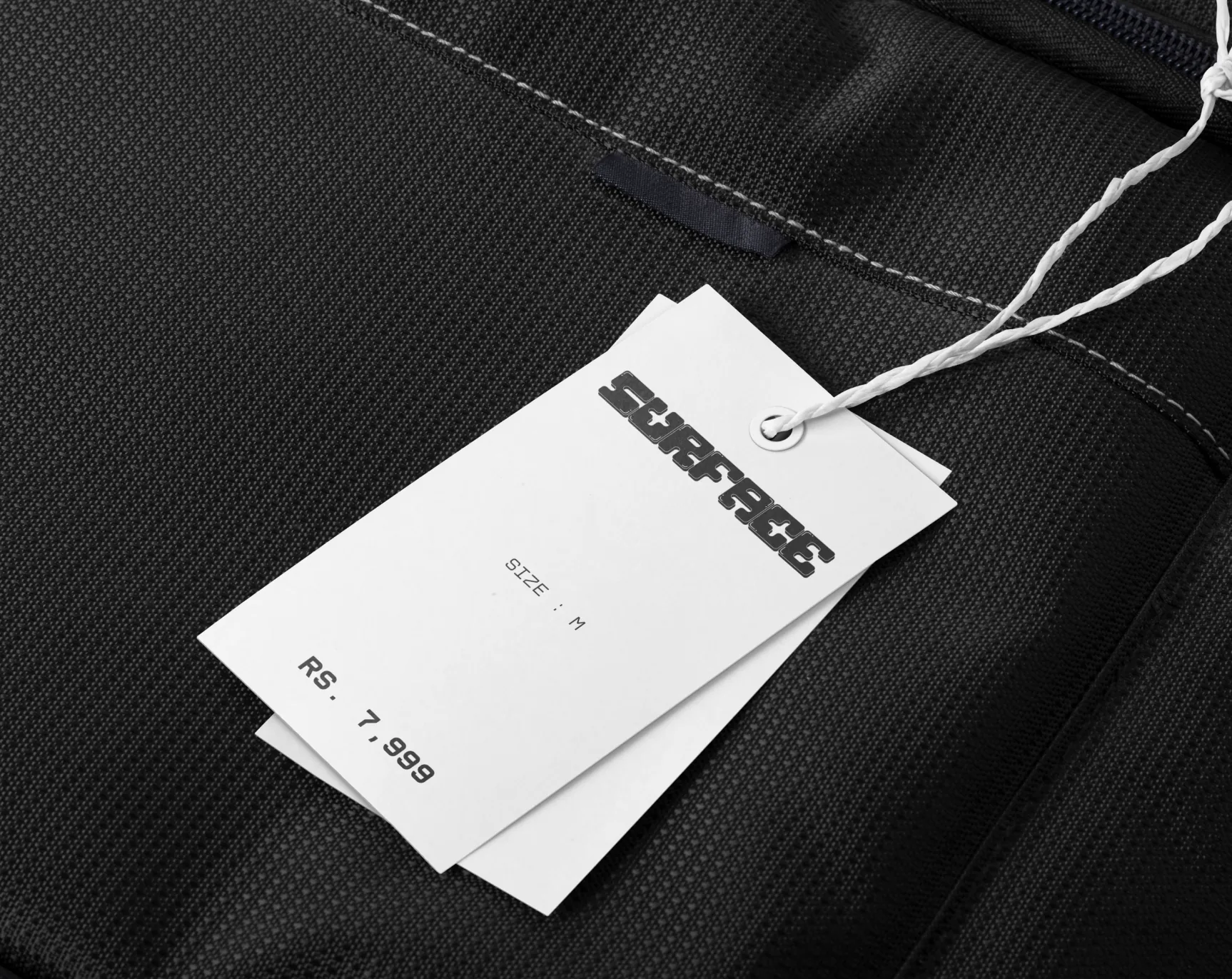 Two white Surface price tags on black fabric.